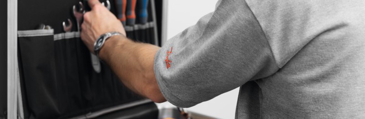 A photo of a contractor in a short sleeved shirt, grabbing tools out of a large toolbox featuring boxed Danfoss products inside.