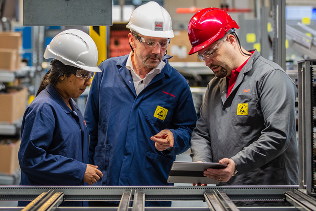 Parceiro da DrivePro segurando um iPad e explicando algo para dois clientes em uma fábrica