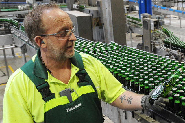 Homem inspecionando uma garrafa de HEINEKEN ao lado da linha de engarrafamento