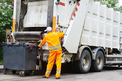 A garbage truck starring a garbage man dressed in all yellow loading a dumpster to be disposed representing compaction pressure control solutions by Danfoss