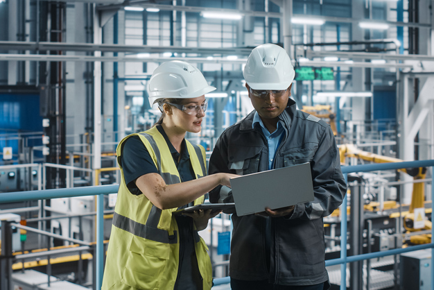 2 people in hard hats looking and pointing at an open laptop